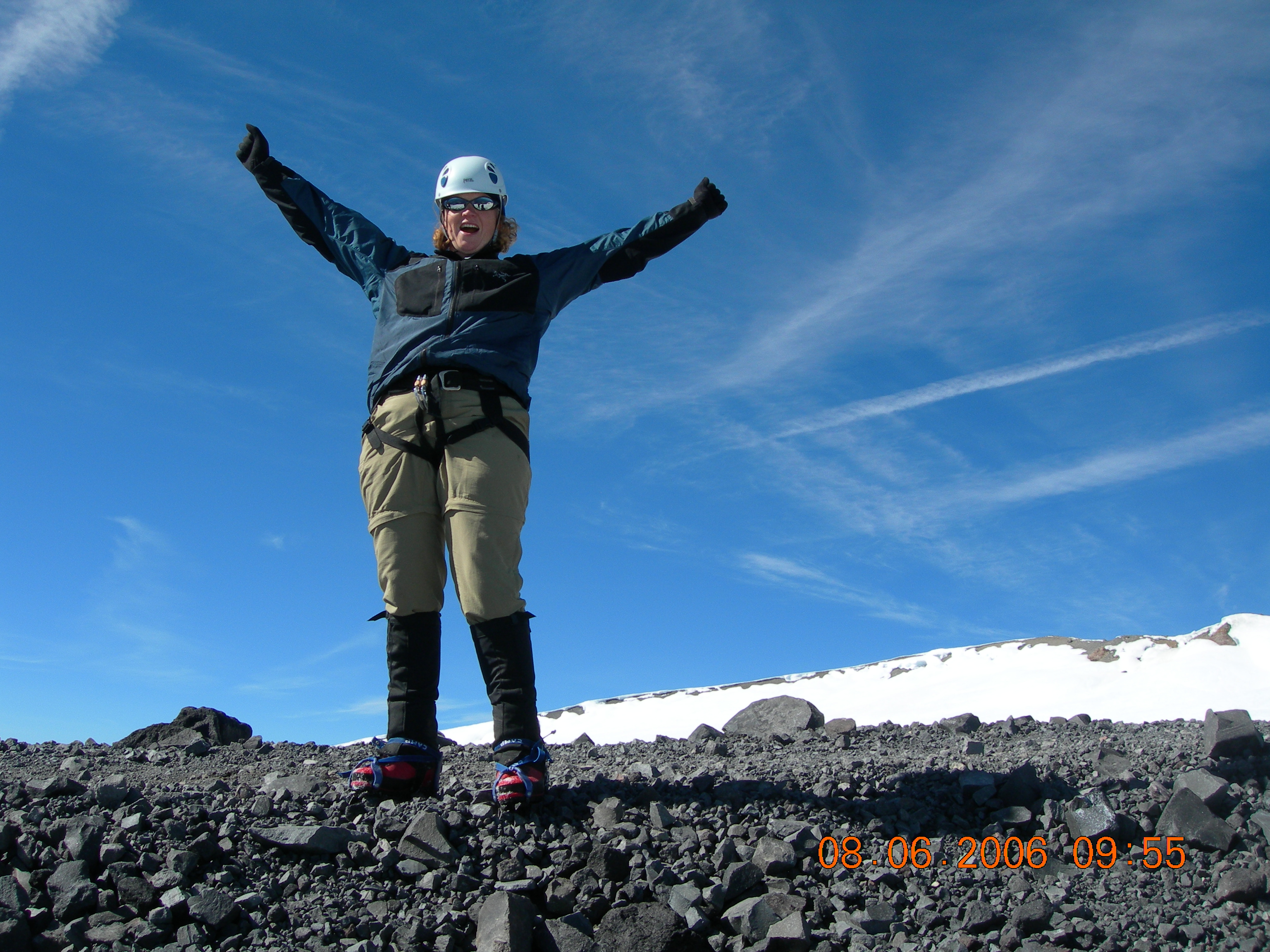 A woman standing on the top of a mountain with her arms in the air. 