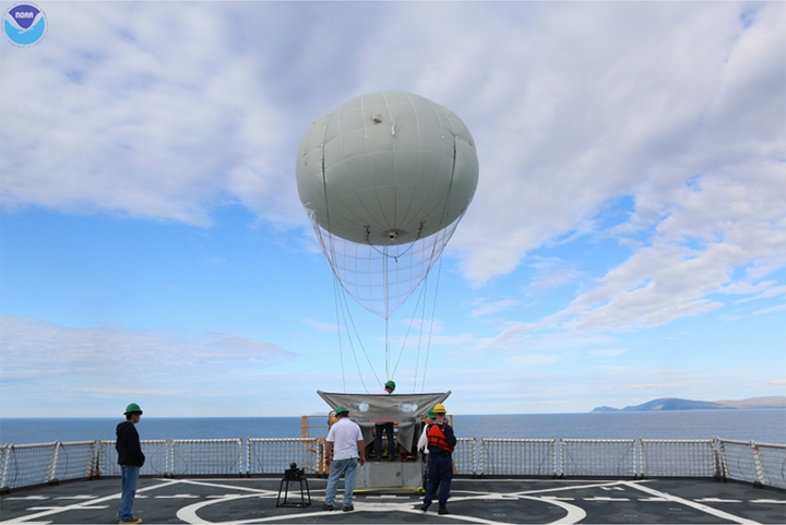 The Aerostat balloon tethered to a ship with people on deck.