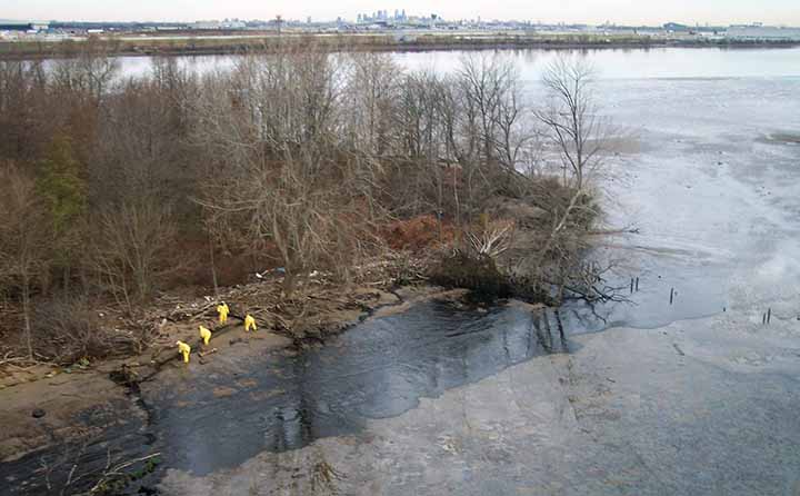 Workers clean oil from an island shoreline on the Delaware River.