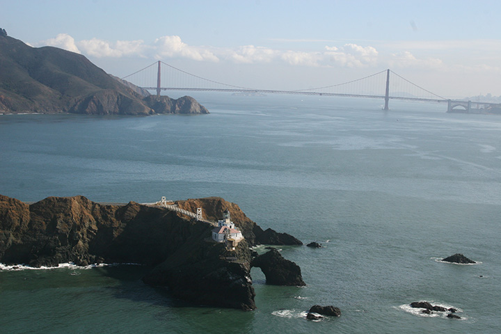 Point Bonita is in the foreground, looking across sheens of lighter colored oil from the Cosco Busan spill and eastward to Golden Gate Bridge and San Francisco Bay.