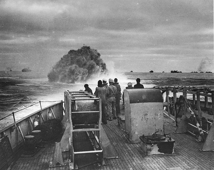 A Coast Guard ship's crew watches an explosion in the water ahead.