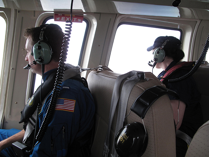 Two Coast Guard observers looking out a helicopter window.