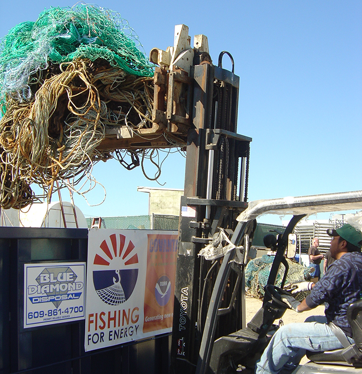Man using a forklift to place old fishing nets in a collection dumpster.