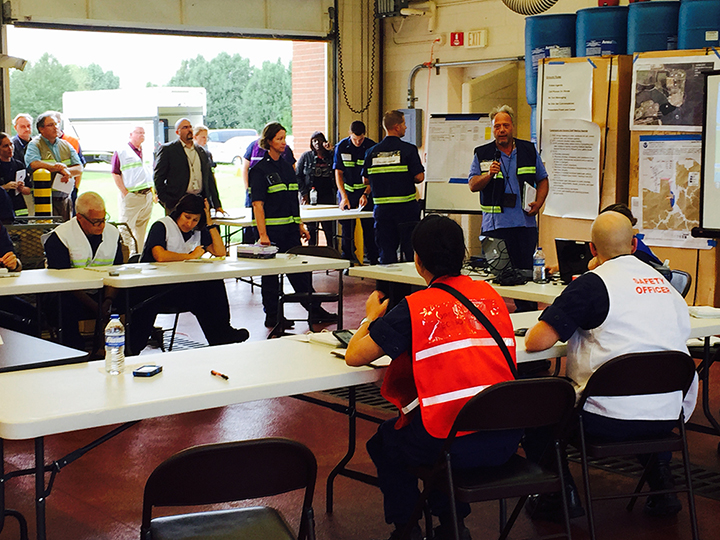 Group of responders in safety vests standing and sitting around tables.