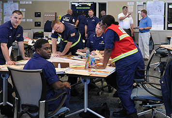 Coast Guard staff standing at tables during a training in the Disaster Response Center.