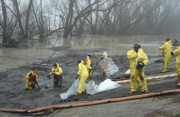 Workers collect oiled debris following an oil spill on a river.
