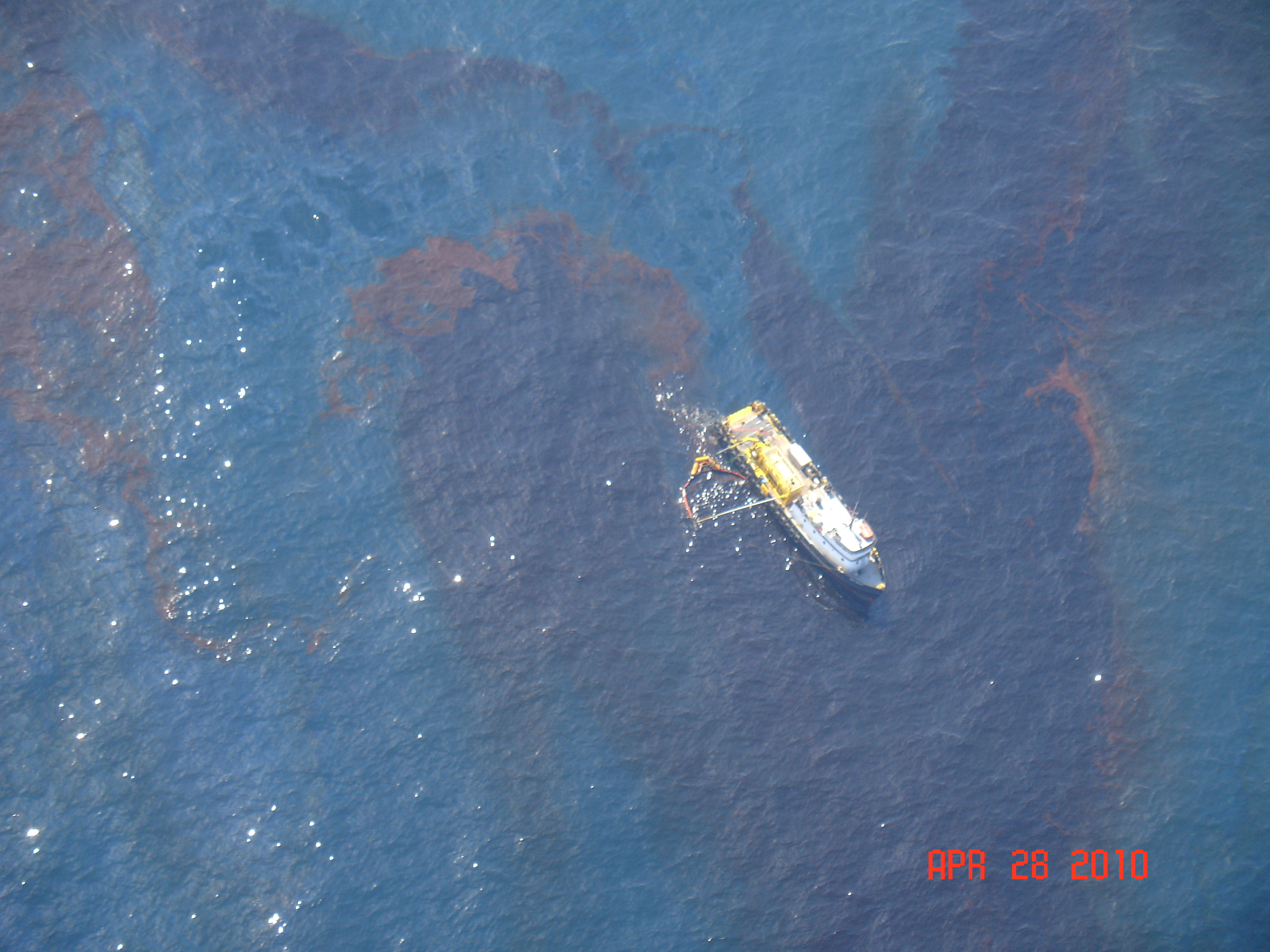 An aerial view of a skimming vessel moving through a patch of oil. 