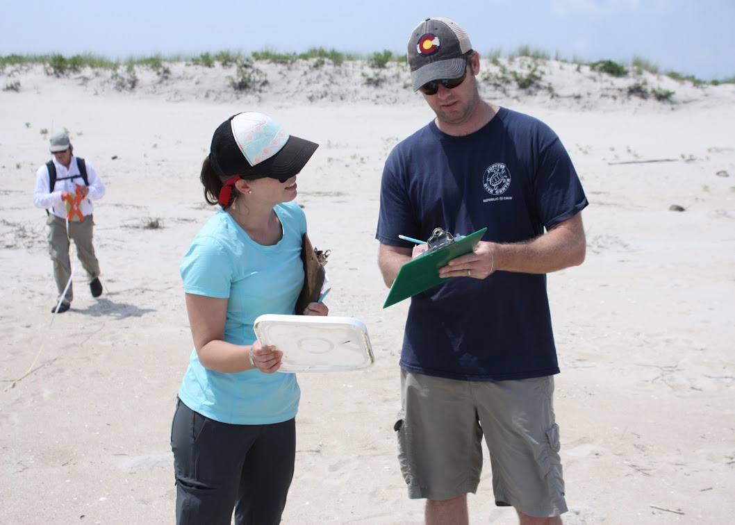 Two people on a beach looking at a clipboard.