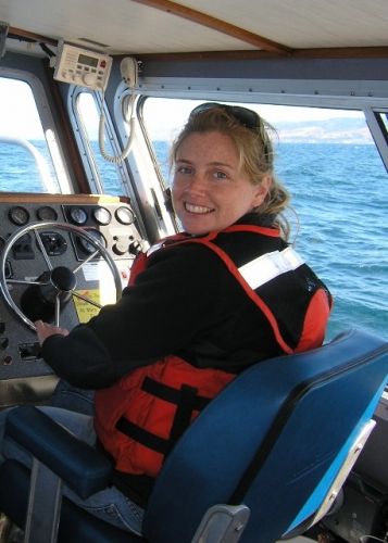A woman in a life jacket steering a boat.