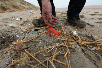 A small orange plastic drift card is picked up from some debris on a beach.