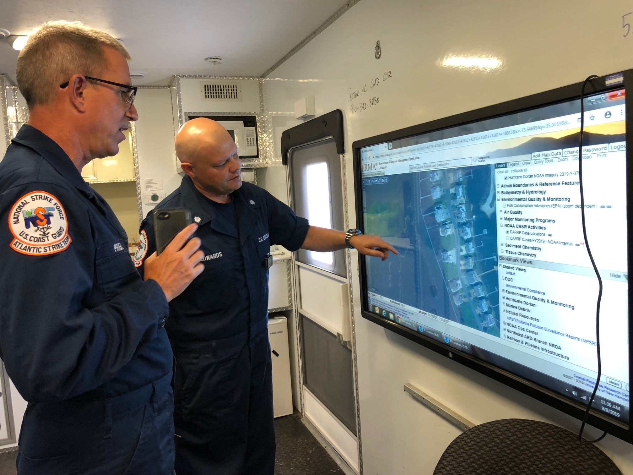 Two people in blue Coast Guard uniforms look at a map on a screen. 