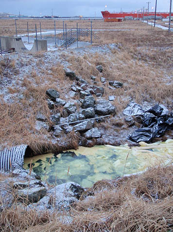 A view of spilled oil next to a culvert in Helmet Creek, with the tanker that supplied the fuel in the background.