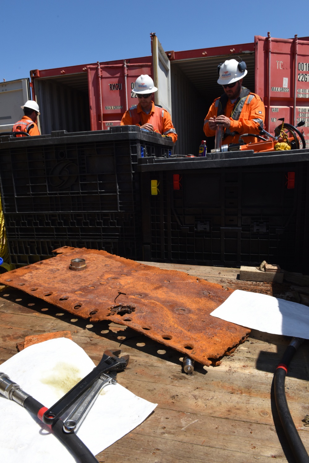 A rusted piece of metal on a ship with several people working in the background.