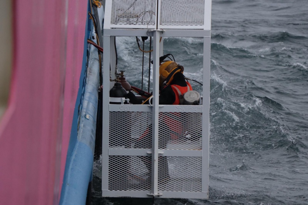A diver being lowered into the water in a diving cage. 