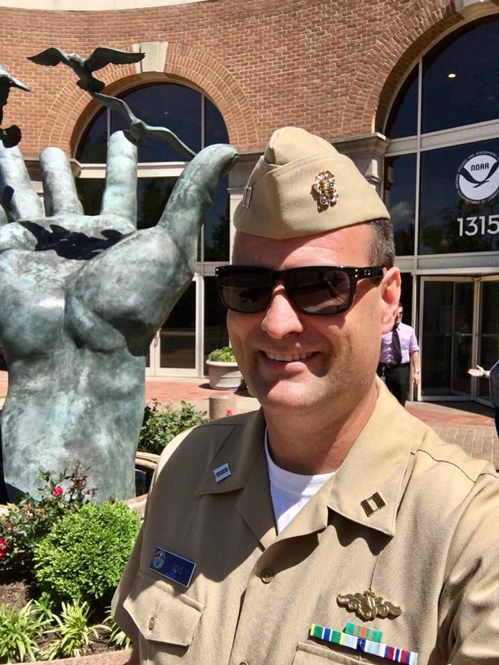 A man in uniform standing in front of a statue of a hand.