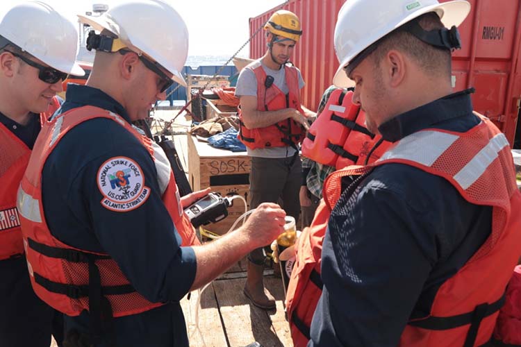 A group of people in life jackets on a boat holding sample jars. 