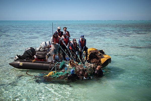 Group in a small boat hauling tangled nets and debris from the water. 