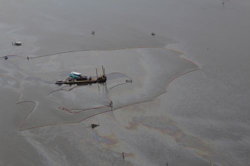 An aerial view of oil contained within pollution boom and skimming vessels surrounded by oil sheens. 