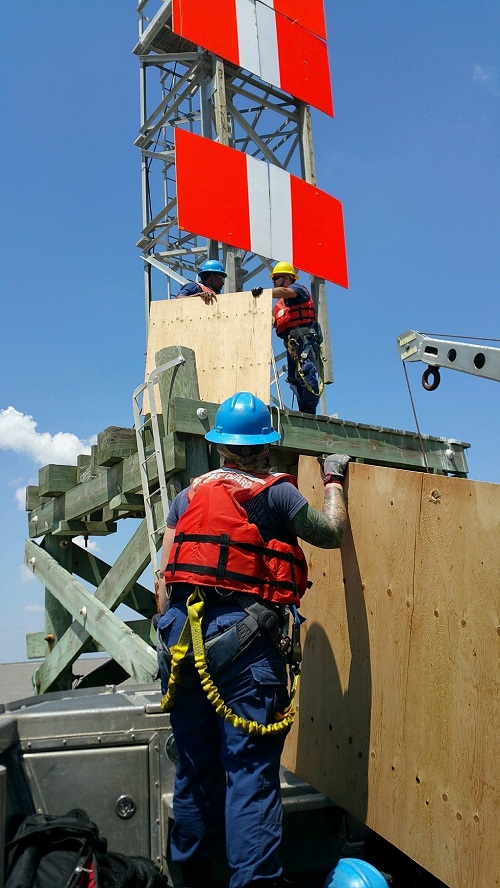 Three men in hard hats lifting large sign onto tower.