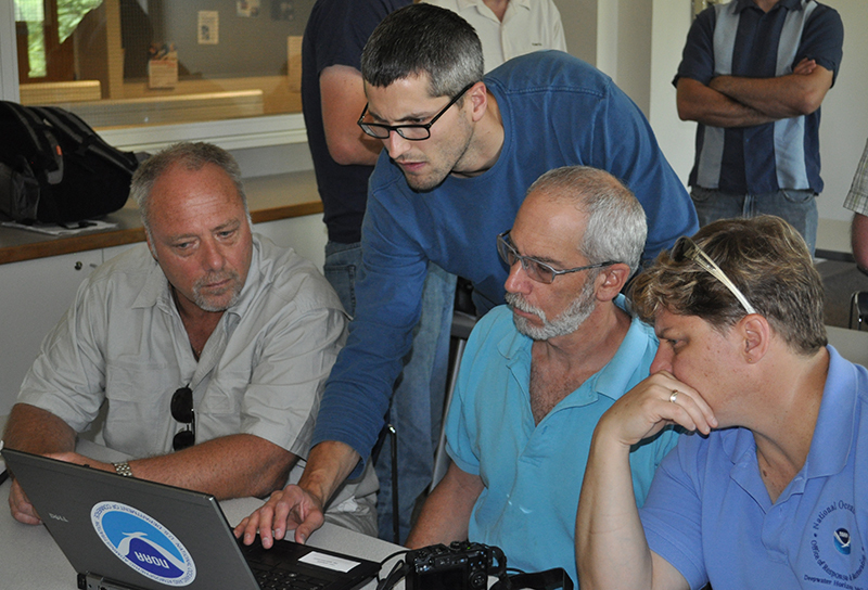 Person instructing three others at a computer screen.