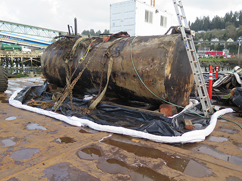 A large damaged tank, surrounded by boom.