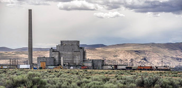 Tall smoke stack and building with mountains in background.