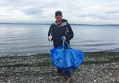 Man with large blue bag standing on a beach.