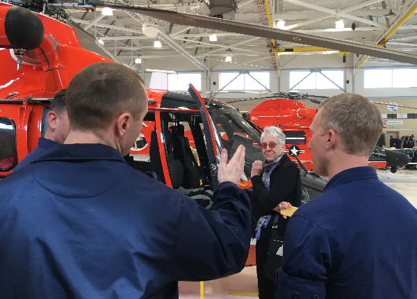 Two men listen as woman speaks next to a helicopter.