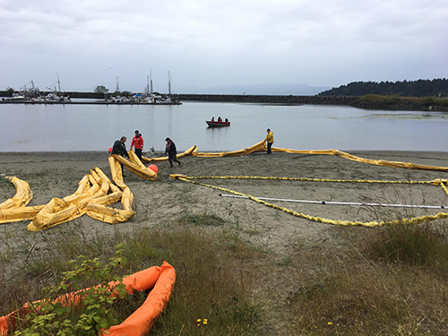 Body of water with workers and boom on a beach.