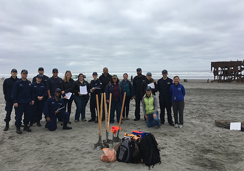 Large group of people pose on a beach next to remnants of a shipwreck.