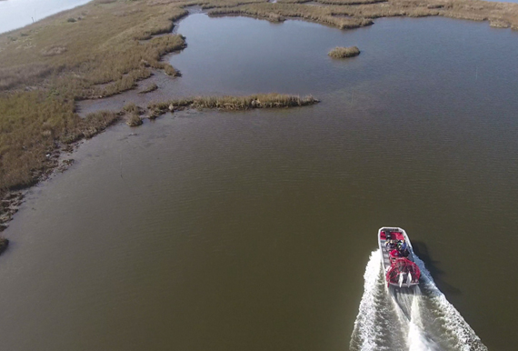 Aerial view of a boat heading towards a marsh.