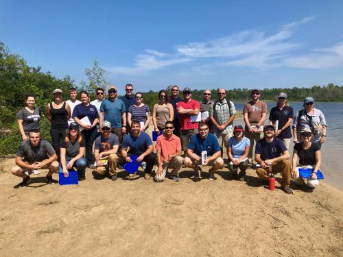 Large group poses for photo on a beach. 