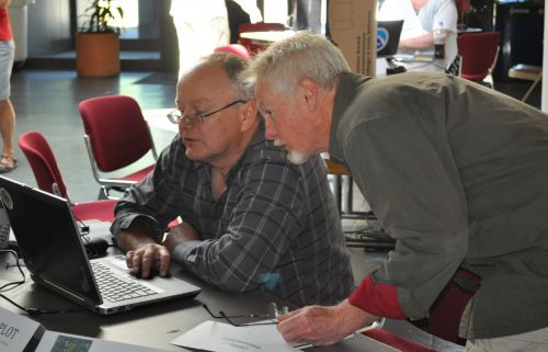 Two men confer over a computer laptop.
