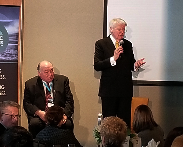 Two men at front of room addressing a group.