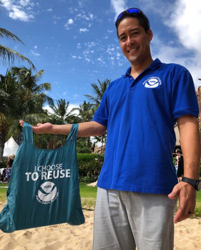 A man holding a reusable bag that reads "I Choose to Reuse."