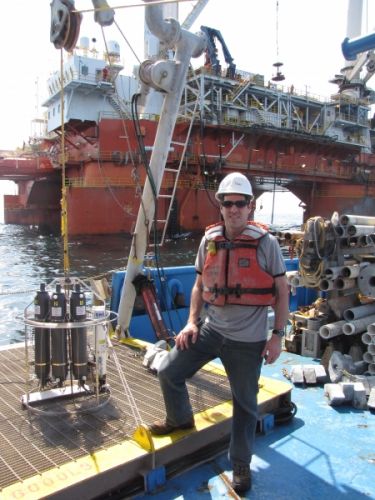 A man in a hard hat and life vest with a vessel in the background.