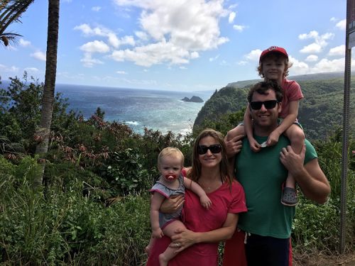 A family of four posing for a photo with a tropical landscape in the background.