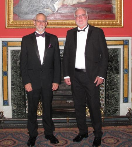 Two men in tuxedos posing for a photo. 