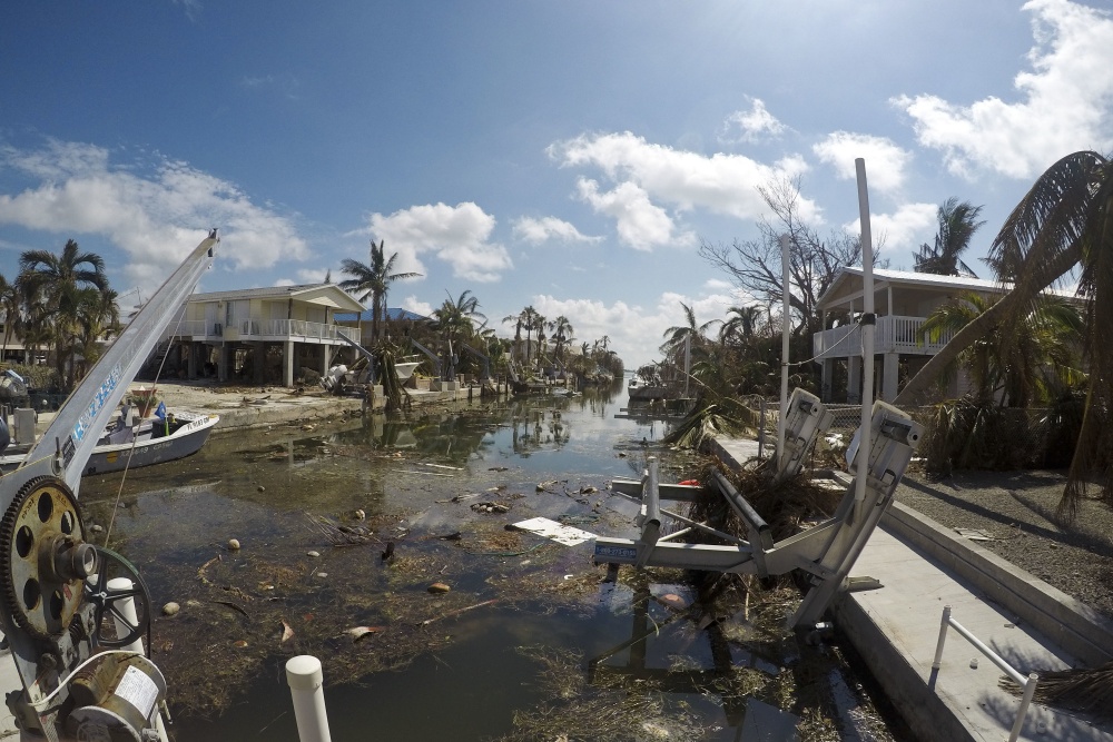 Debris along a canal lined with houses and trees. 