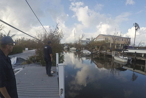 Two men standing on dock next to debris-filled waterway. 