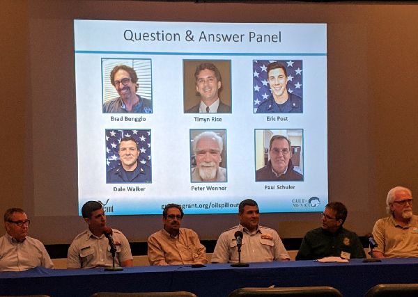 A panel of six men in front of a screen.