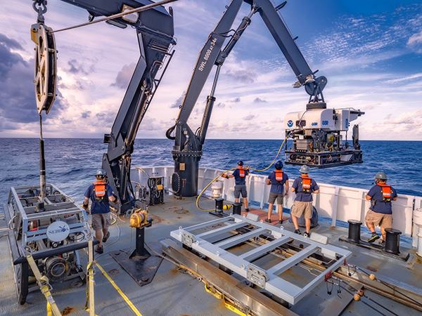 An ROV being lowered into the water by crew on a vessel.