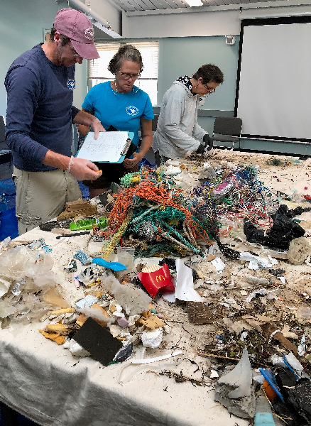 Three people working at a table covered in trash.