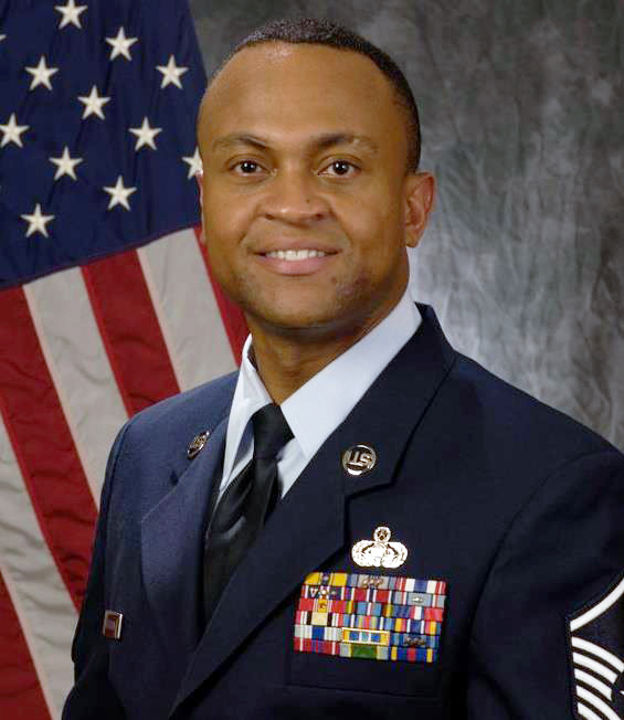 A man in a military uniform in front of a U.S. flag.