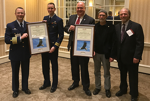 Five men pose for photo; two hold framed certificates. 