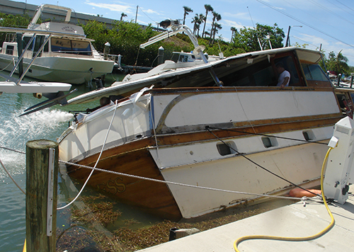 Damaged boat in the water, leaning partially against a dock.