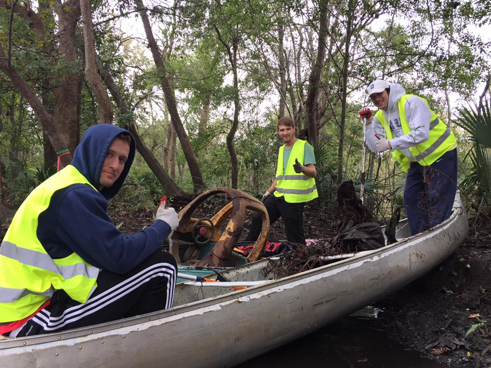 Three people in and around a canoe with debris.