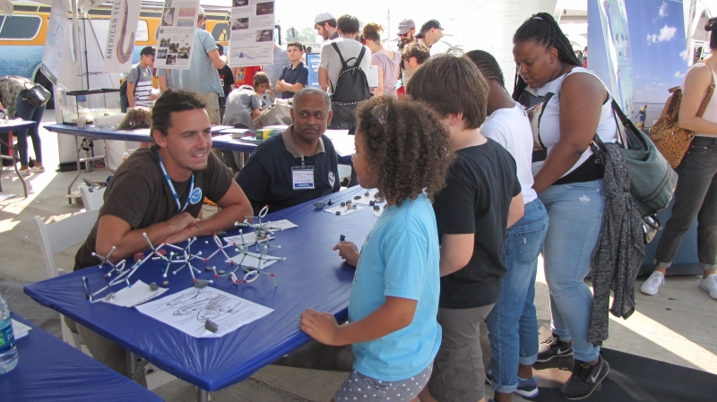 Children speaking with NOAA presenters at a table.