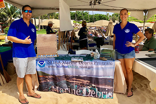 Man and woman standing at an outdoors exhibit table. 