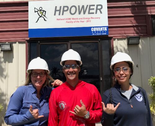 Three people pose in front of a sign.